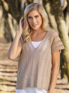 a beautiful blonde woman standing in front of trees wearing a knitted top and jeans