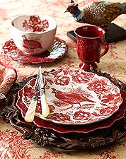 the table is set with red and white plates, silverware, and two bird figurines