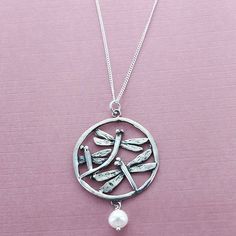 a silver necklace with dragonflies and a pearl hanging from it's center on a pink background