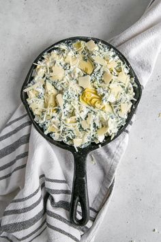 a skillet filled with cheese and spinach on top of a white table cloth