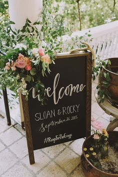 a welcome sign with flowers and greenery on it