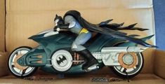 a batman figurine sitting on top of a toy motorcycle in a cardboard box