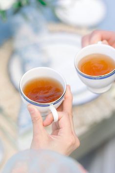 two people holding cups of tea in their hands