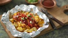 some food that is sitting in tin foil on a cutting board next to utensils