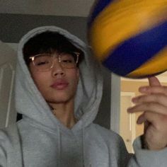 a young man wearing glasses and a hoodie holds up a ball in front of his face