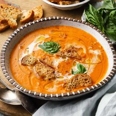 two bowls of tomato soup with bread croutons and spinach on the side