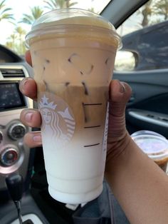 a person holding up a starbucks drink in their hand while sitting in a car with the steering wheel behind them