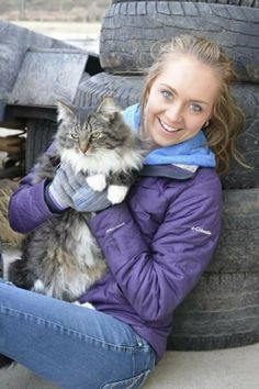 a woman holding a cat in her arms while sitting next to an old truck tire