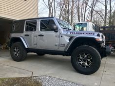 a gray jeep parked in front of a house next to a truck with the word rubicon on it