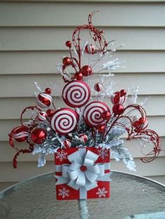 a red and white christmas tree with candy canes on it's top, sitting on a table in front of a house