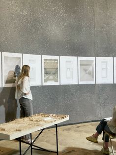 two people are sitting at a table and looking at pictures on the wall behind them