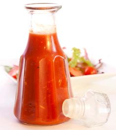 a glass bottle filled with ketchup next to a salad