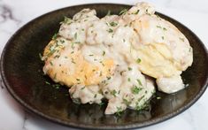 a black plate topped with biscuits covered in gravy and garnished with parsley