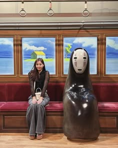 a woman sitting on a bench next to a large animal statue in front of a window