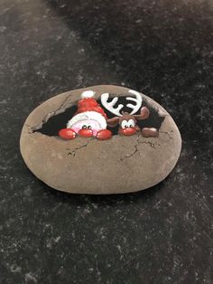 there is a rock painted with santa claus and reindeers in the hole on it