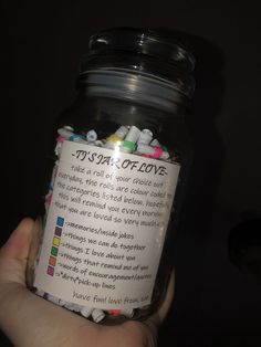 a person holding a jar filled with lots of colorful beads and writing on the label