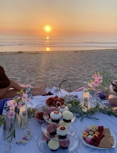 two people sitting at a table with cupcakes and cakes in front of the ocean