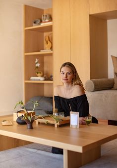 a woman sitting at a wooden table in front of a book shelf with books on it