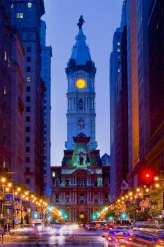 a clock tower towering over a city filled with tall buildings at night, lit up by street lights