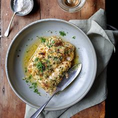 a white plate topped with chicken covered in sauce and parsley on top of a wooden table