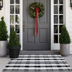 a gray door with a red ribbon on it and two potted plants next to it