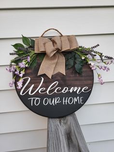 a welcome sign hanging from the side of a house with flowers and greenery on it