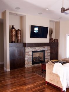 a living room with wood flooring and a flat screen tv mounted above the fireplace