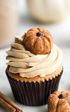 two cupcakes with icing and chocolate chips on top are sitting next to cinnamon sticks