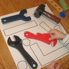 a child's hand holding a pair of scissors next to tools on top of a piece of paper