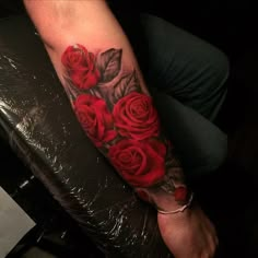 a woman's arm with red roses and leaves tattooed on the forearm, sitting on a chair