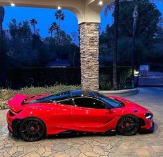 a red sports car is parked in front of a building with palm trees at night