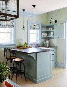 a kitchen with blue cabinets and an island in the middle is decorated with hanging lights