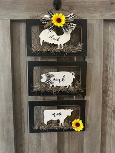 three black and white farm signs with sunflowers on them hanging from the side of a barn door