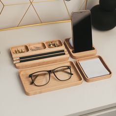 an iphone, glasses and pen on a desk with a phone in the holder next to it