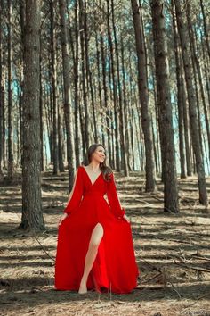 a woman in a long red dress is standing among the trees and looking up into the sky