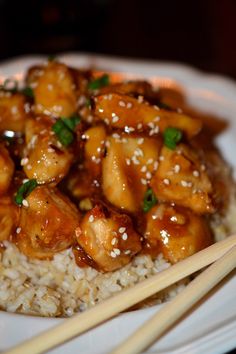 a white plate topped with chicken and rice next to chopsticks on a table