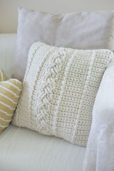 a white crocheted pillow sitting on top of a couch next to two yellow pillows