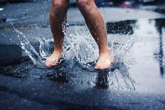 a person standing on top of a puddle with their feet in the air while it rains