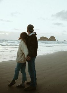 a man and woman standing on top of a beach next to the ocean