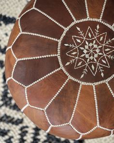 a brown leather ottoman with an intricate design on it's top and beading around the edges