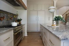 a kitchen with white cabinets and marble counter tops, gold pulls on the doors and brass knobs