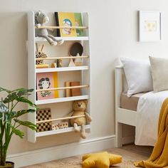 a white book shelf filled with lots of books next to a bed and potted plant