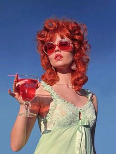 a woman with red hair and sunglasses holding a drink