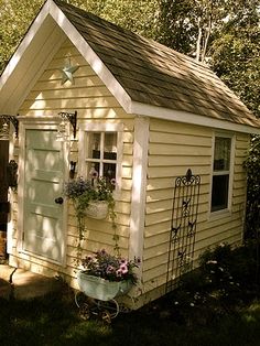 a small yellow house with flower pots on the front door and window boxes in the back