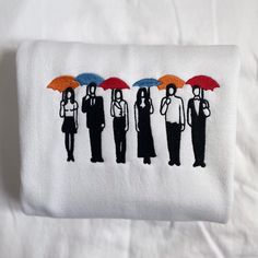 three people with umbrellas embroidered on a white cloth pillow case that is sitting on a bed