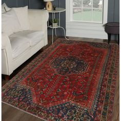 a large red rug in a living room next to a white couch and window with blue walls