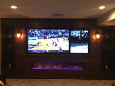 two large televisions mounted on the wall in a living room with fireplace and entertainment center