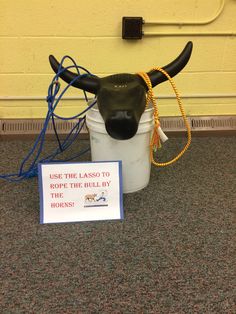 a bull's head sitting on top of a bucket next to a sign that says use the lass to rope the bulls by horns