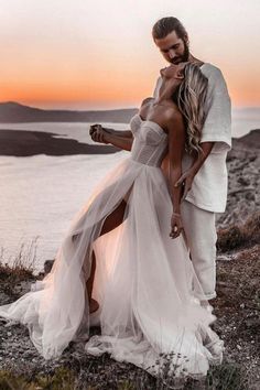 a man and woman standing next to each other on top of a hill near the ocean