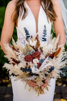 a woman in a wedding dress holding a bouquet with feathers and flowers on it's side